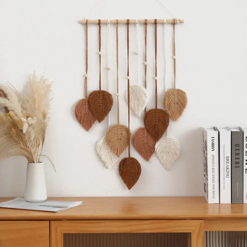Decorative wall hanging with leaf-shaped objects on a wooden shelf against a white wall.