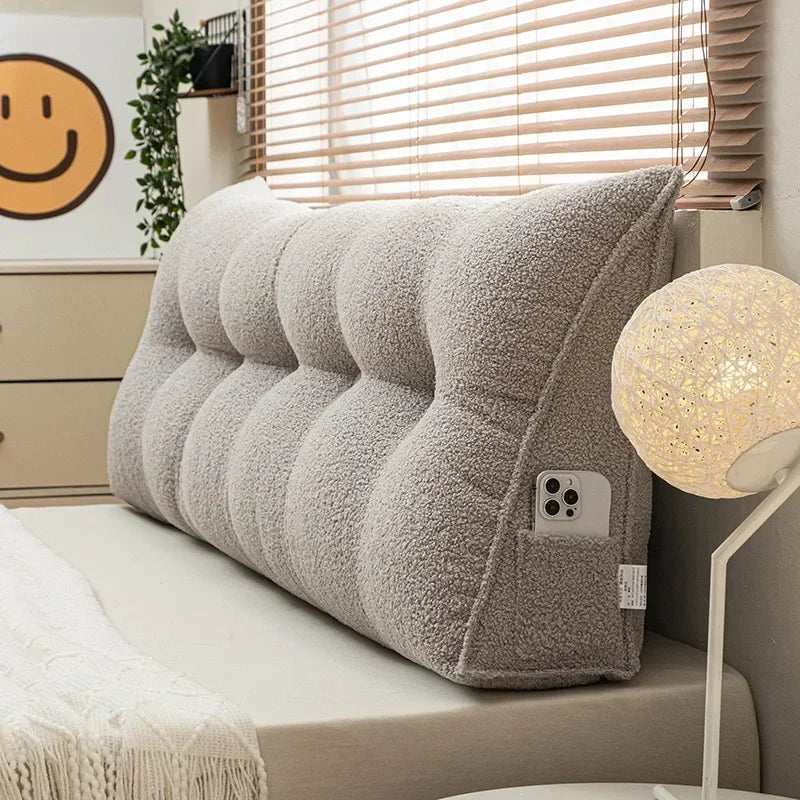 Gray plush headboard pillow on a bed with a smiley face decoration in the background