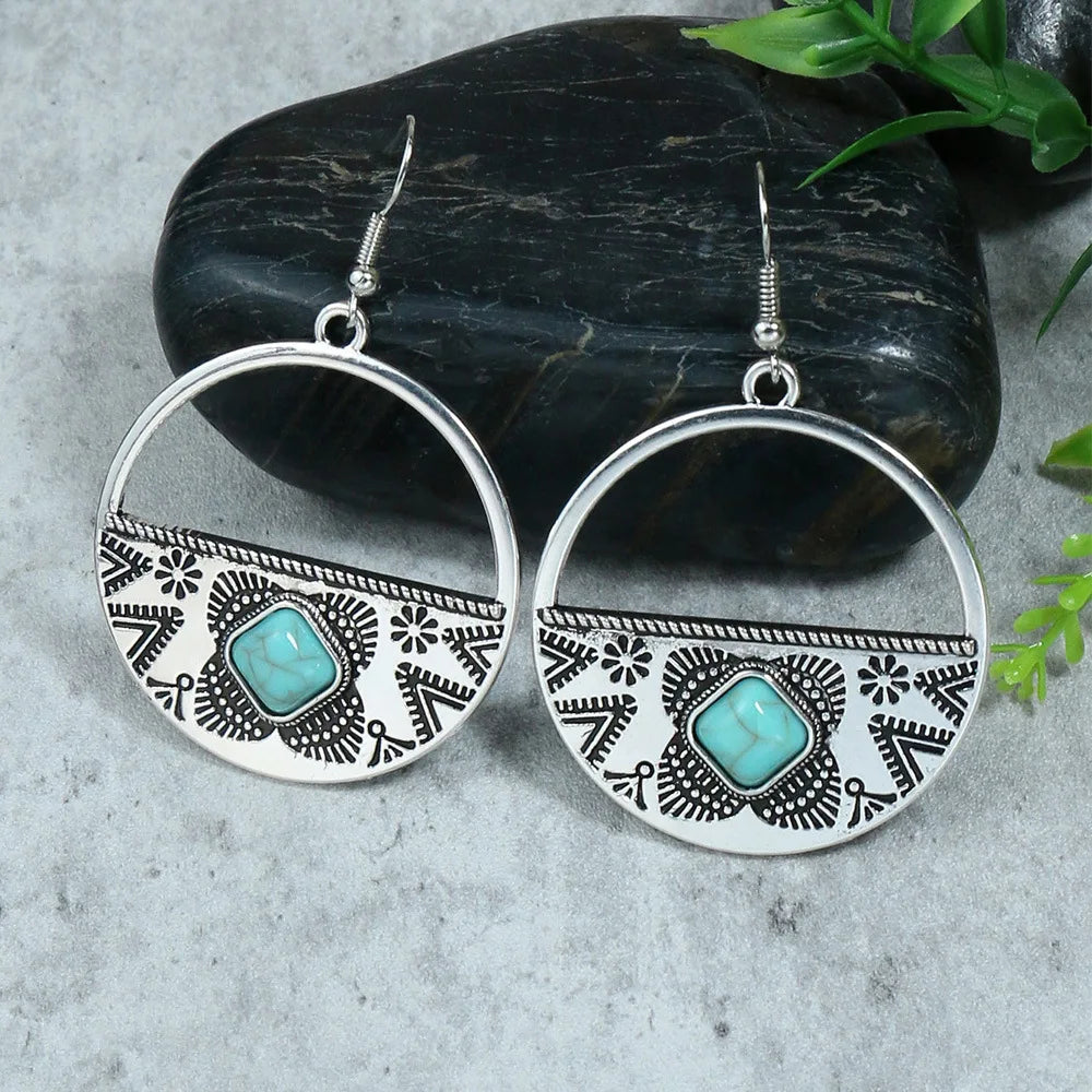 Silver hoop earrings with turquoise stones on a stone surface