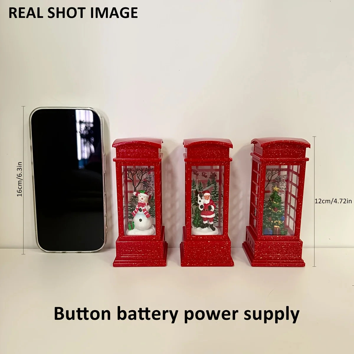 Three red decorative phone booths with Christmas scenes next to a smartphone for scale on a white background.