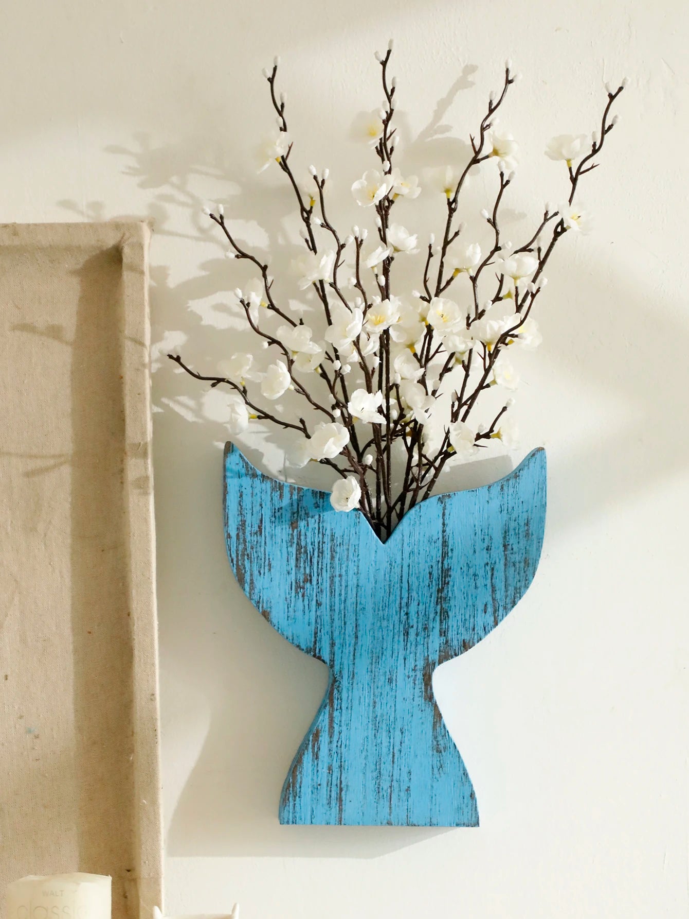 Blue whale tail wooden vase with rustic distressed finish, styled with white blossom branches as coastal home decor displayed on the wall