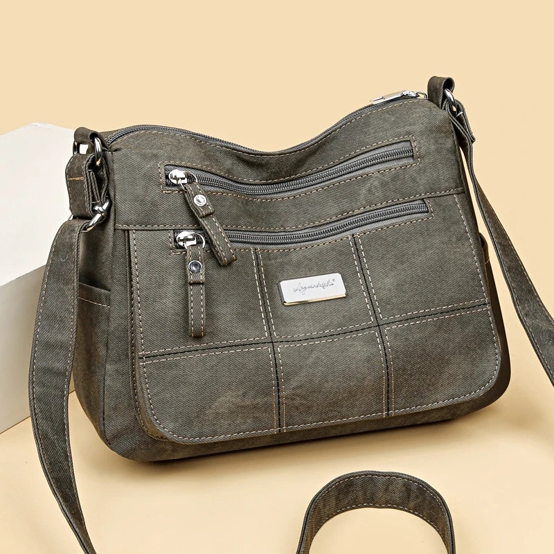 Gray shoulder bag with multiple zippers on a beige background