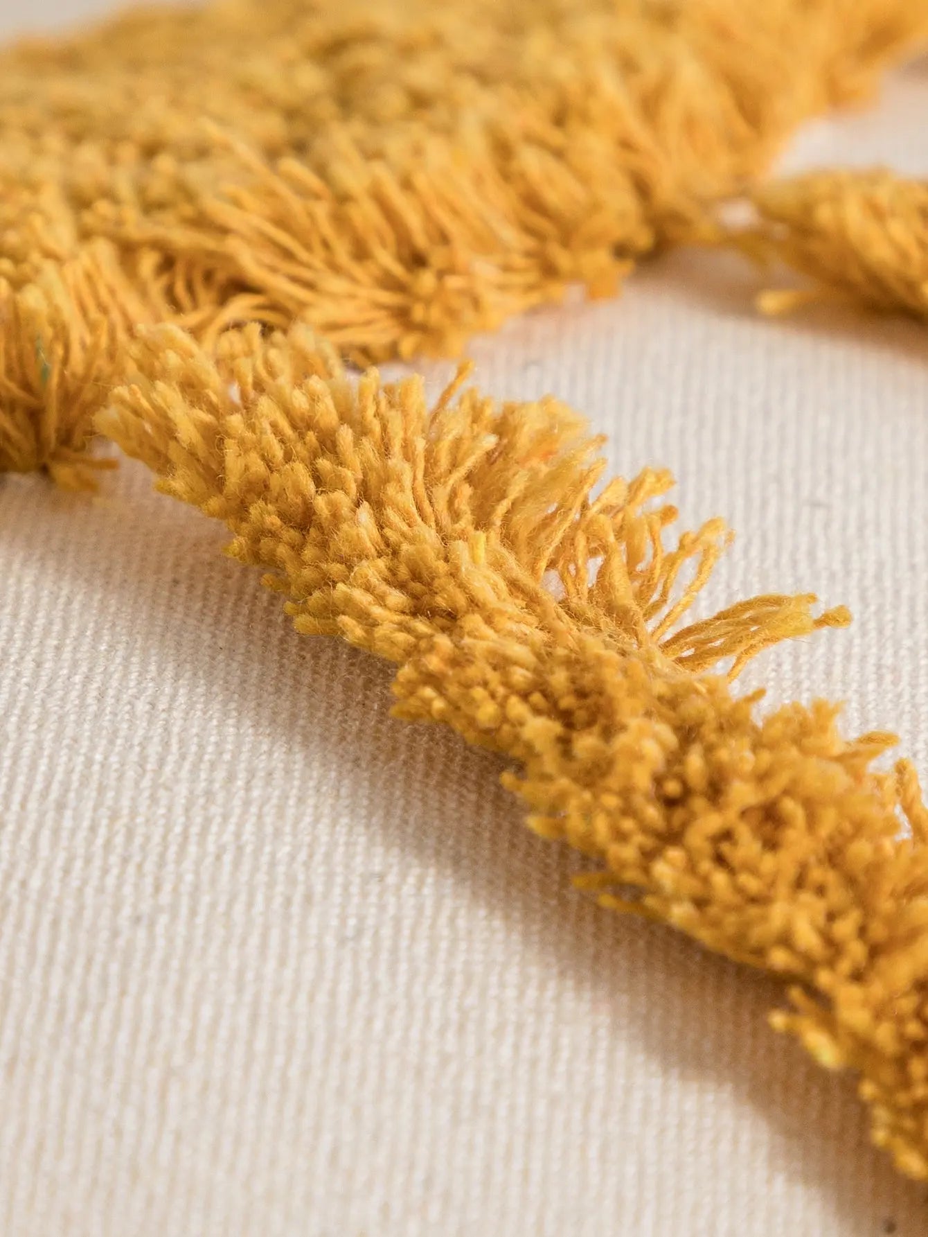 Close-up of a mustard yellow fabric with fringes on a beige background