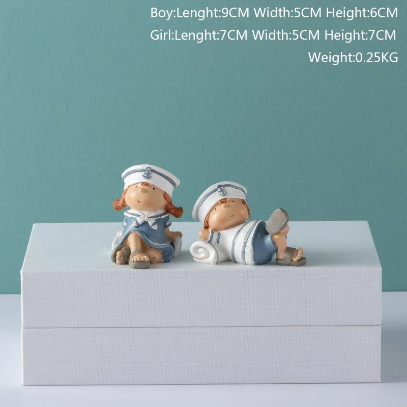 Two ceramic figurines of a boy and girl in sailor outfits on a white box with a light blue background.