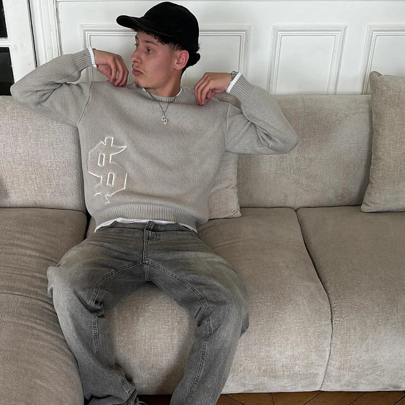 Person sitting on a beige couch wearing a gray sweater and black cap.