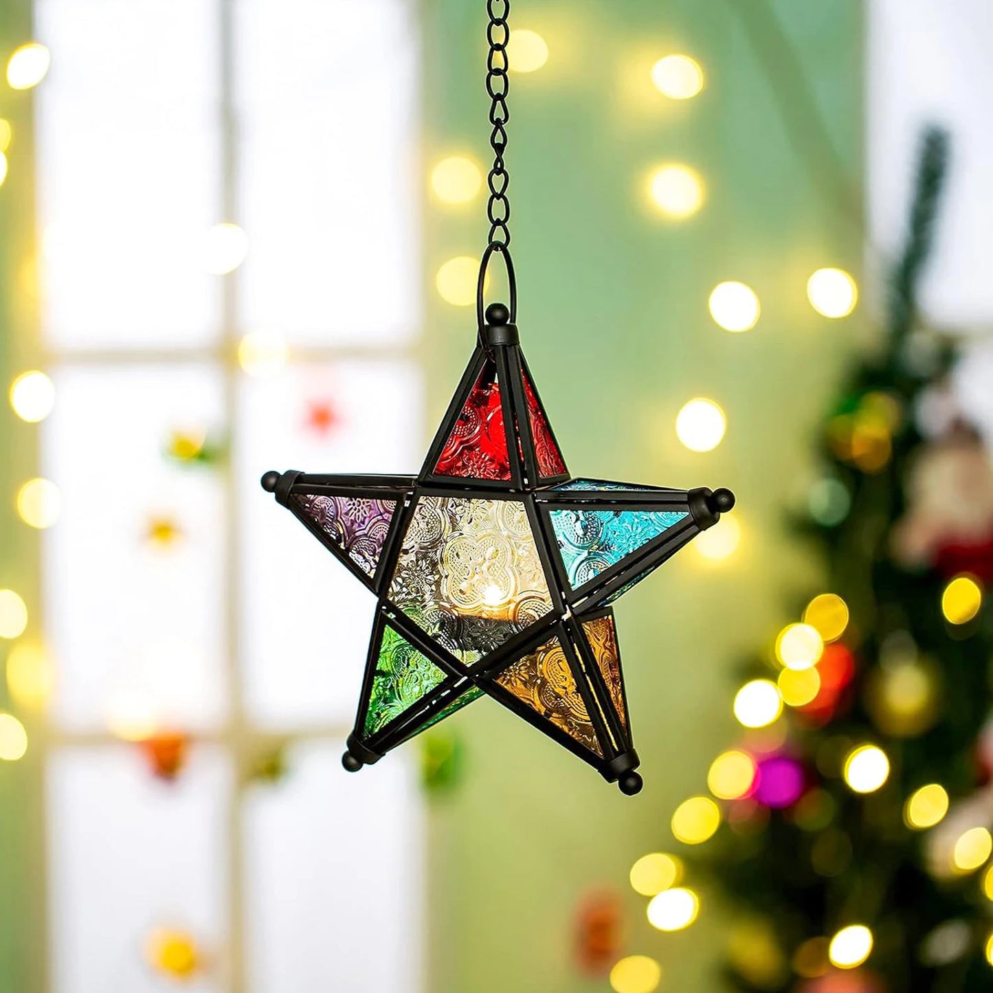 Star-shaped stained glass ornament with colorful facets hanging against a festive background with lights and a Christmas tree.