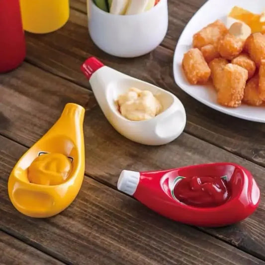 Two condiment dipping bowls, one yellow and one red, with a small white container of sauce on a wooden table.