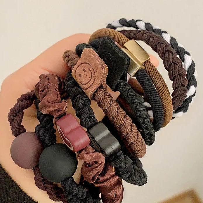 Collection of braided hair ties with various designs held in a hand against a neutral background.