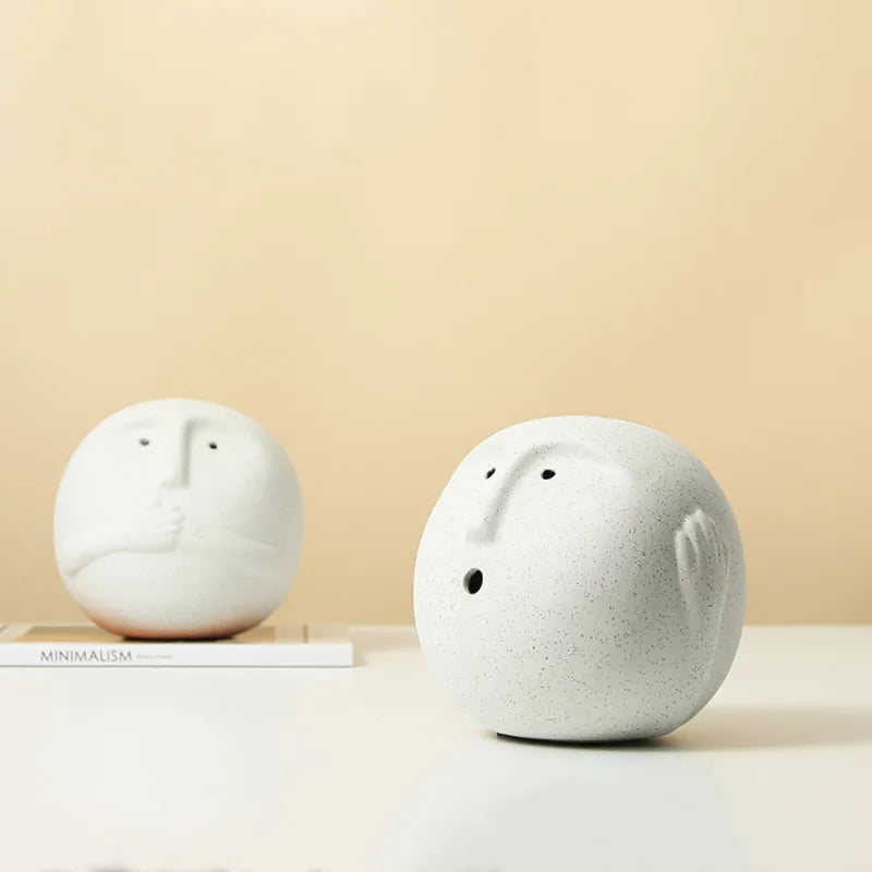 Two white ceramic face-shaped objects on a beige background