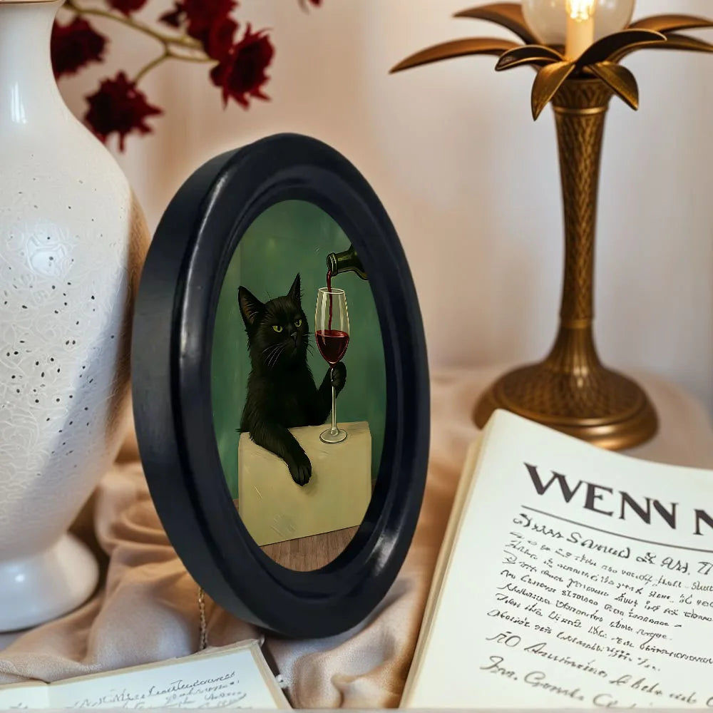 Framed picture of a black cat with a glass of wine on a decorative surface with a vase and lamp.