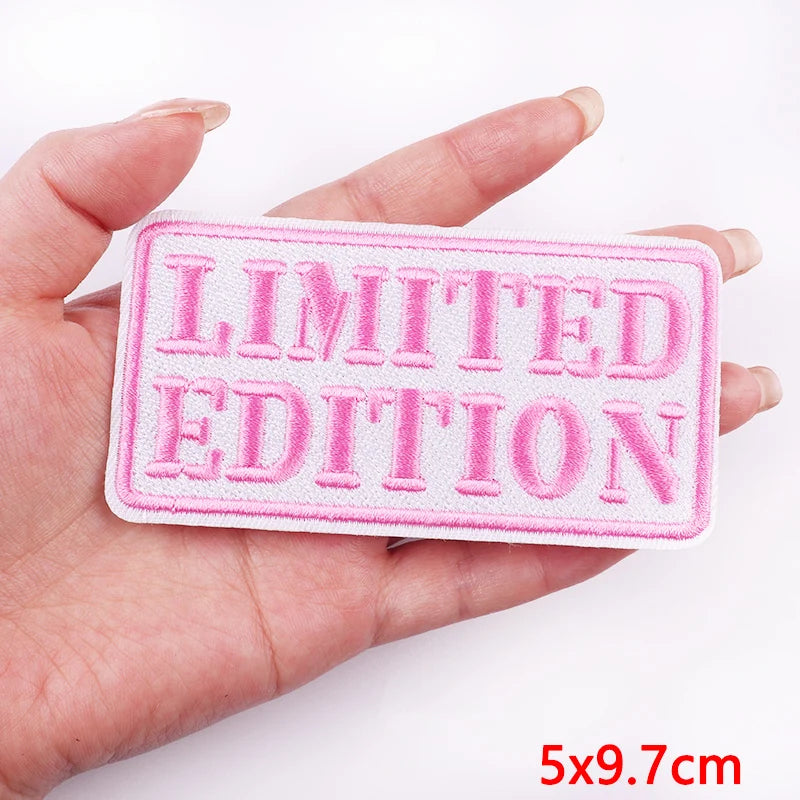 Pink 'LIMITED EDITION' patch held by a hand on a white background