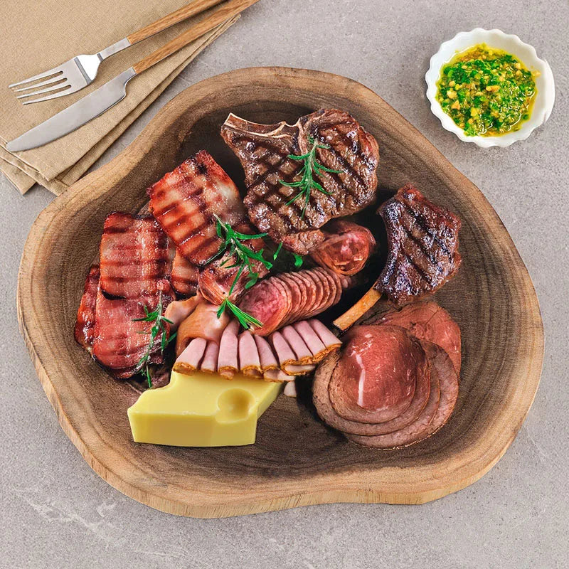 Assorted meats including steaks, sausages, and ham on a wooden platter with a side of cheese.