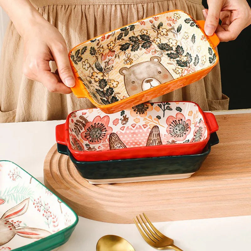 Stack of ceramic baking dishes with floral and bear designs on a wooden surface.