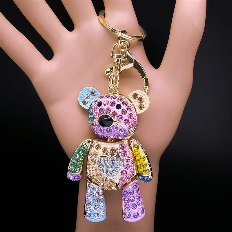 Colorful teddy bear keychain held in a hand against a black background