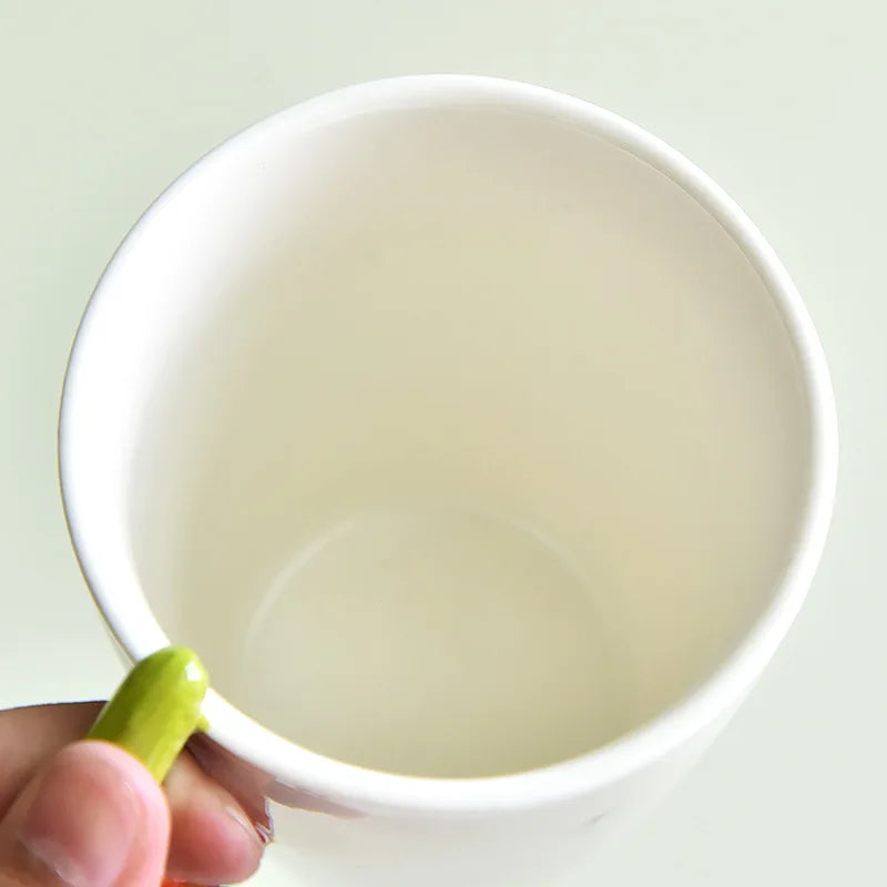 White mug with a green handle held by a hand on a light green background