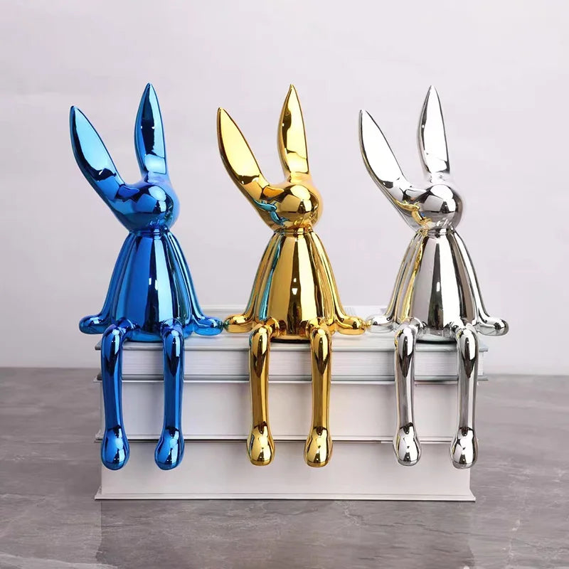 Three metallic rabbit sculptures in blue, gold, and silver on a white base.