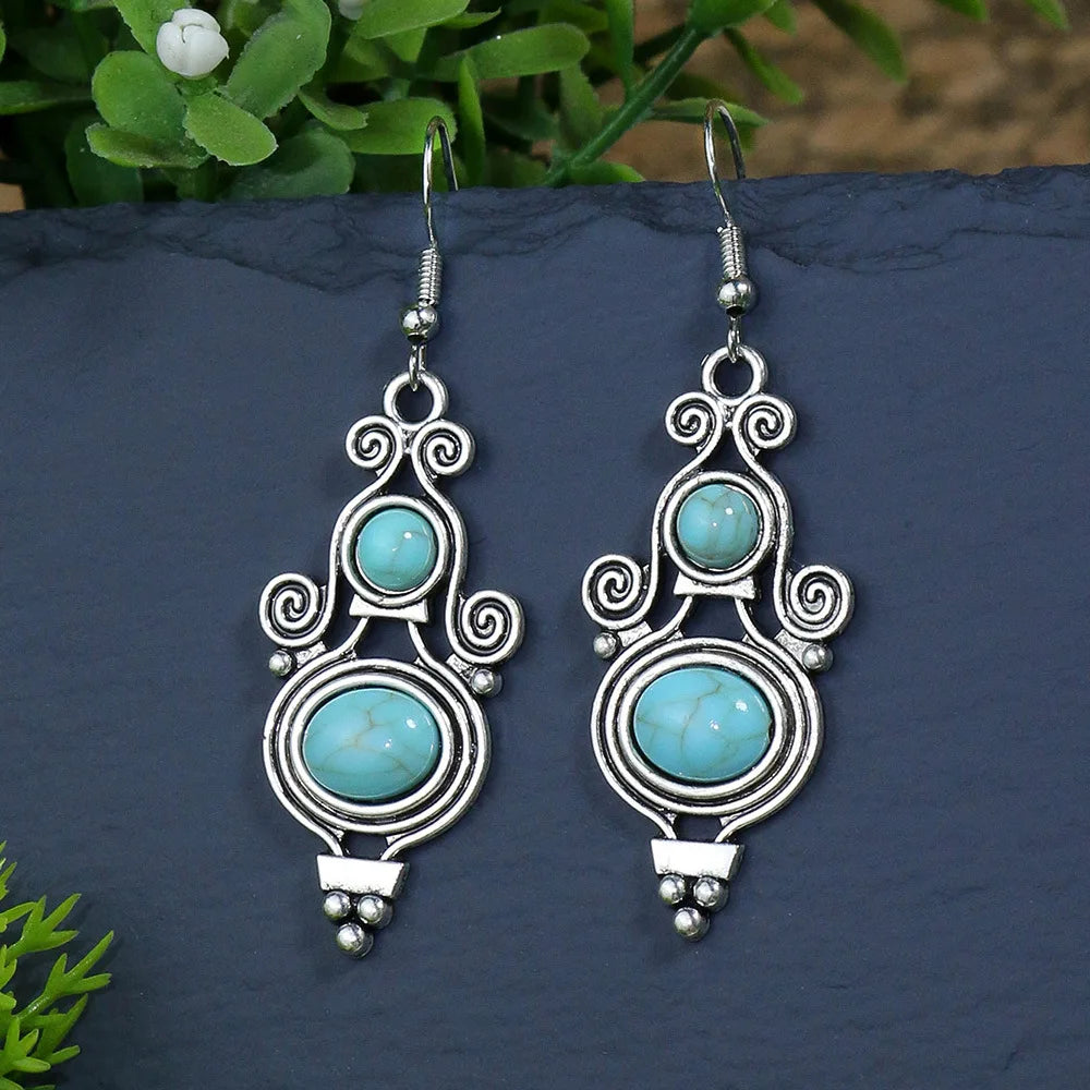 Silver earrings with turquoise stones on a dark surface with greenery.