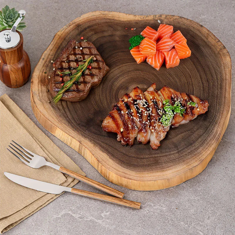 Grilled meat dish with vegetables on a wooden plate, accompanied by a fork and knife.