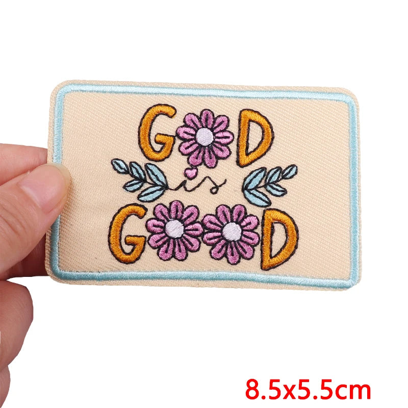 Embroidered patch with 'Good' text and flowers held by a hand, size 8.5x5.5cm.
