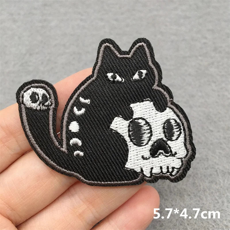 Black and white cat skull patch held by a hand on a gray background