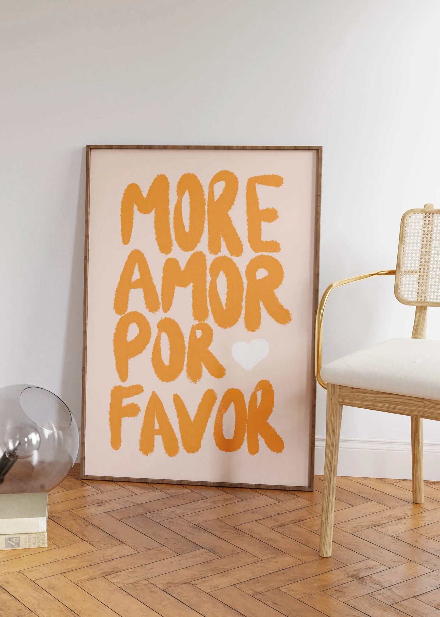 Framed artwork with 'More Amor Por Favor' text in a room with a chair and decor items.