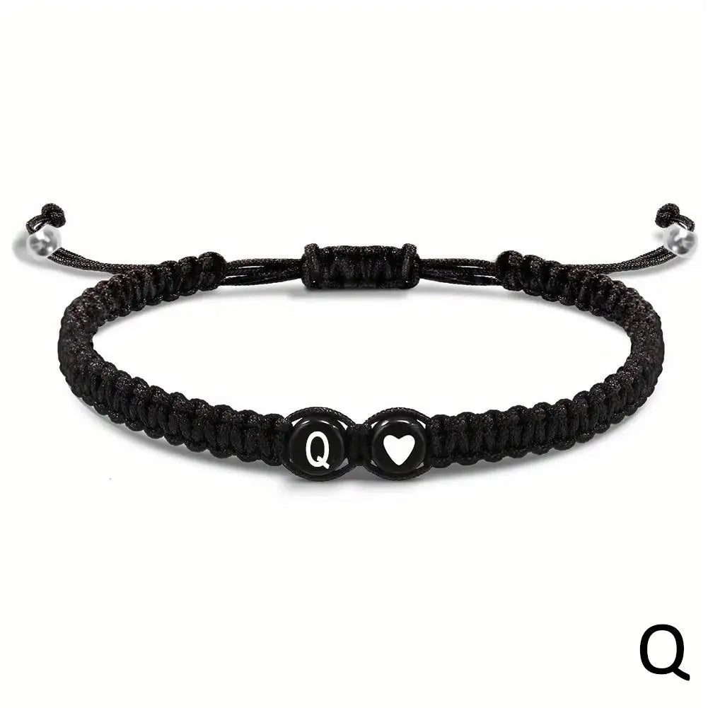 Black braided bracelet with a heart and letter 'Q' charm on a white background