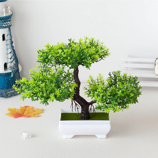 Artificial bonsai tree in a white pot on a light surface with a decorative item in the background.
