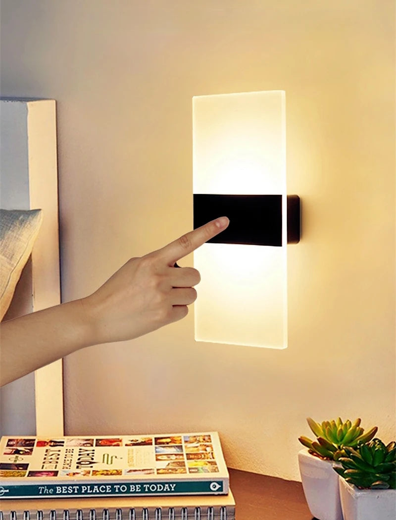 Person pointing at a wall-mounted light fixture in a room with a magazine and plant.