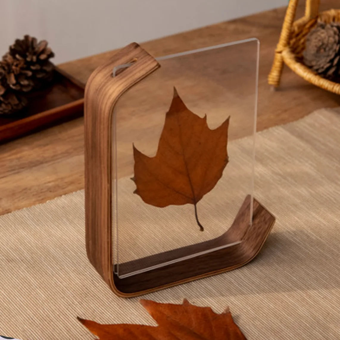 Wooden photo frame with a clear acrylic cover displaying a pressed leaf on a wooden surface.