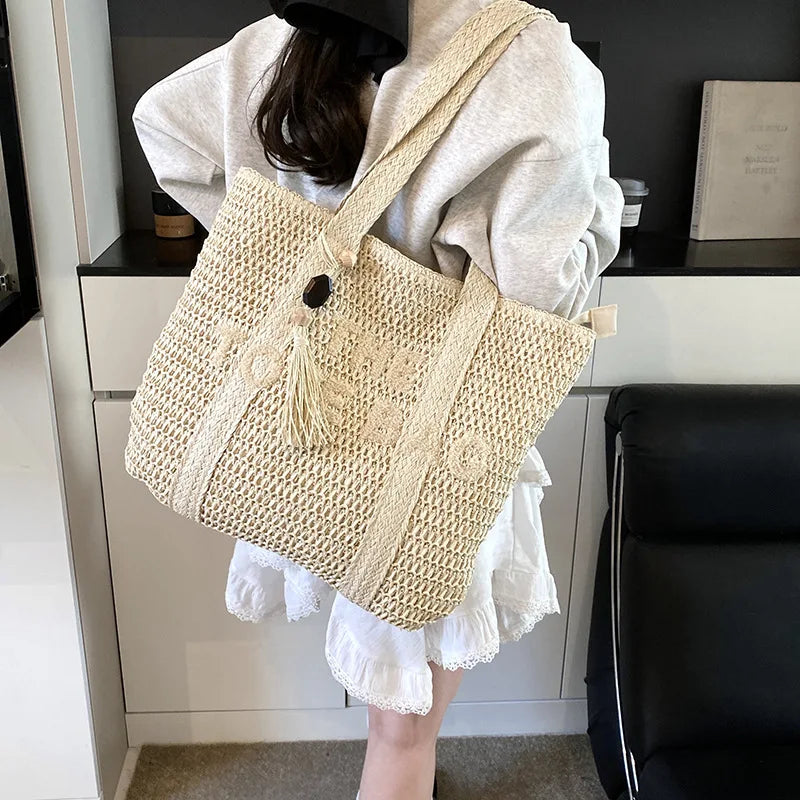 Person holding a beige woven bag with a black button and tassel in an indoor setting.