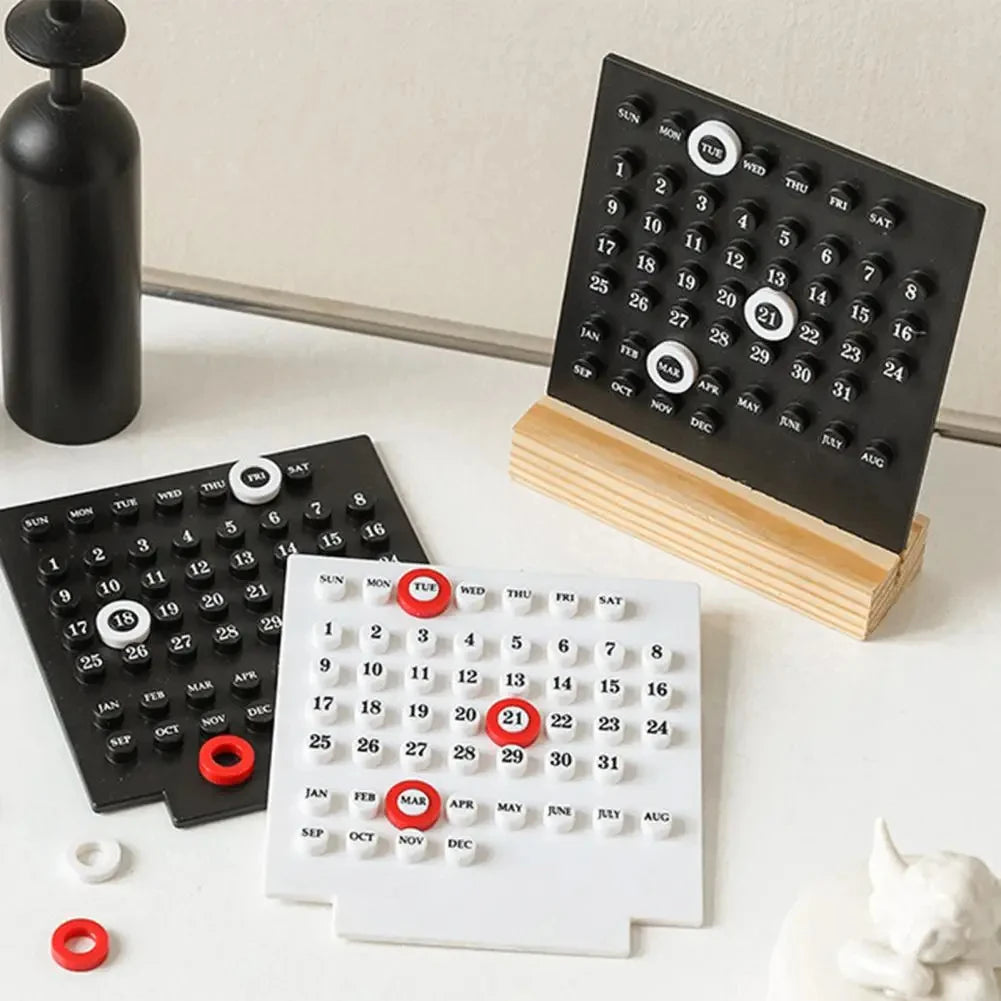 Black and white calendar designs on a light surface with a black vase and white sculpture in the background.