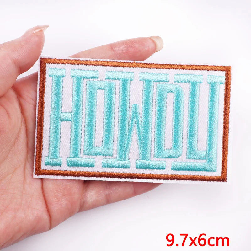 Embroidered patch with 'HOWDY' text held in a hand, on a white background