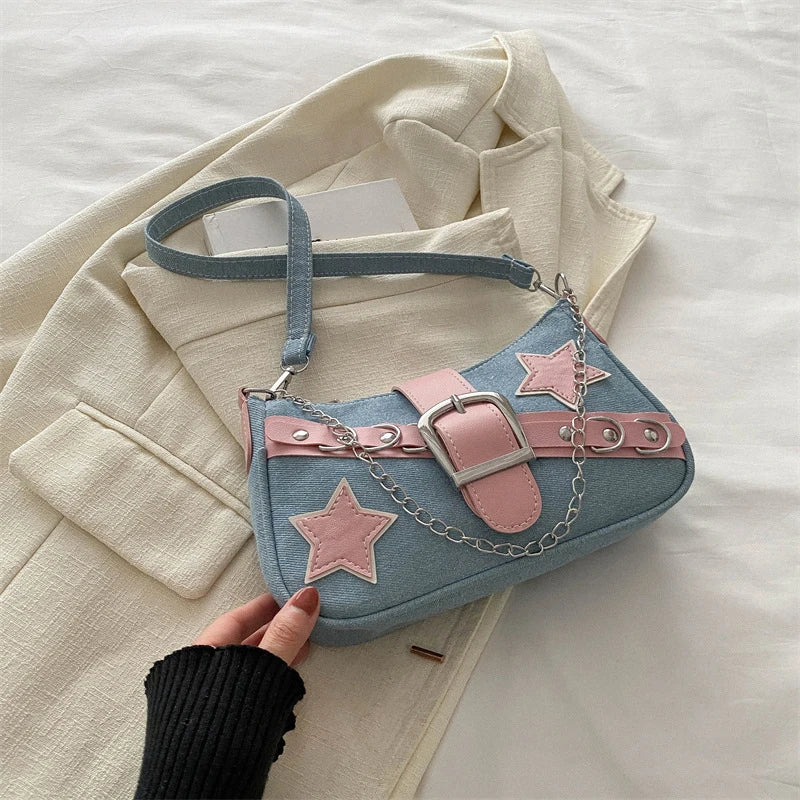 Blue handbag with pink stars and belt design held by a hand on a light-colored fabric background