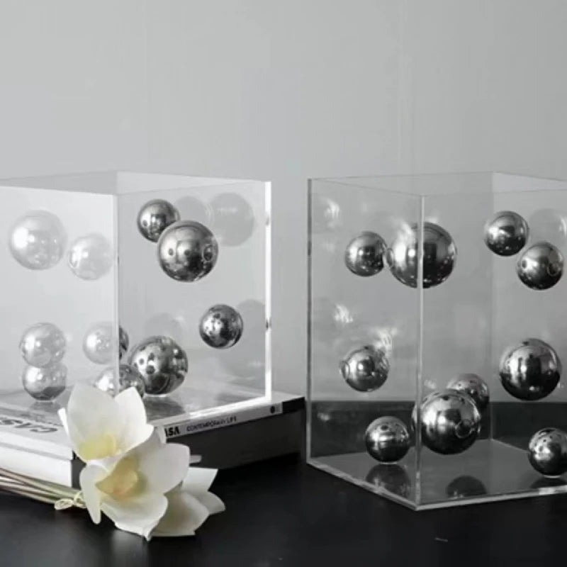 Silver mirrored spheres suspended inside transparent acrylic cube sculptures on a tabletop.