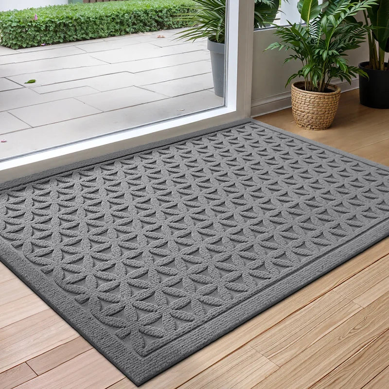 Gray doormat with leaf pattern on a wooden floor, leading to a glass door.