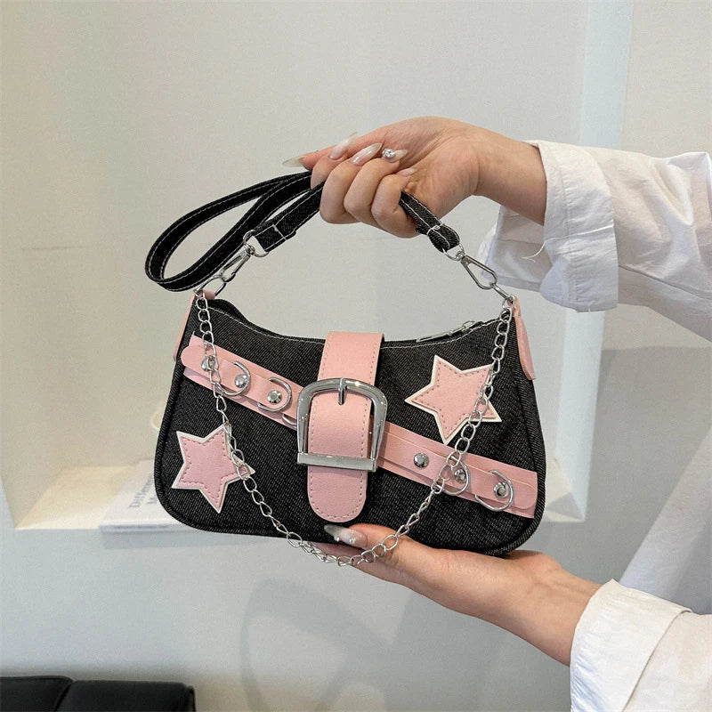 Black handbag with pink accents and star designs held by a person against a neutral background