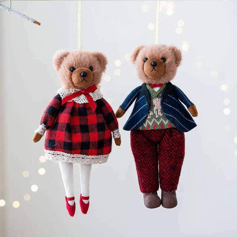 Two teddy bears, one in a red and black checkered dress and the other in a blue and red outfit, hanging against a light background.