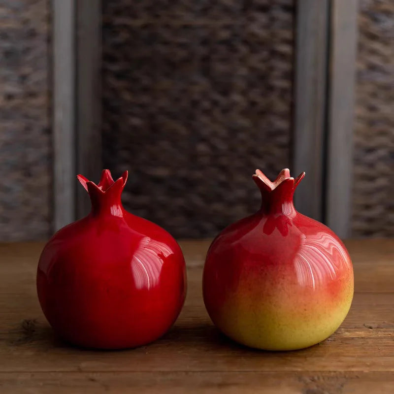 Two red ceramic pomegranates on a wooden surface with a textured wall background.