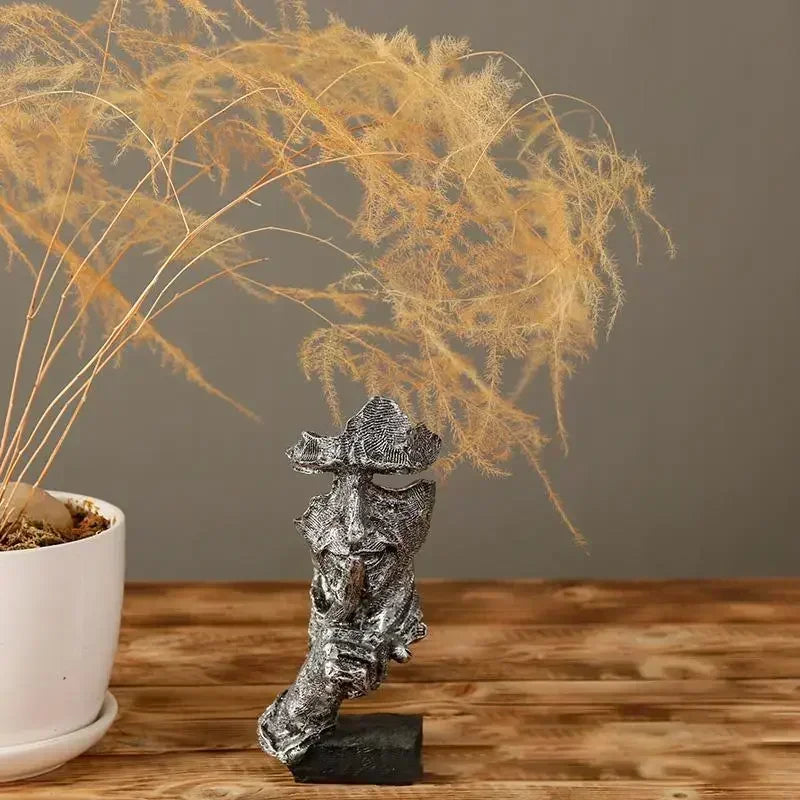 Decorative silver sculpture on a wooden surface with a plant in the background