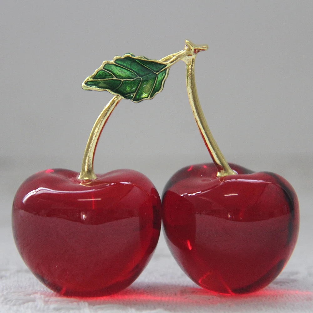 Two red cherry ornaments with gold stems and green leaves on a light gray background
