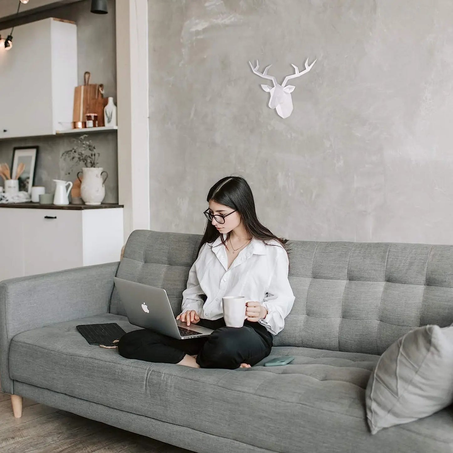 Woman sitting on a gray sofa using a laptop in a modern living room.