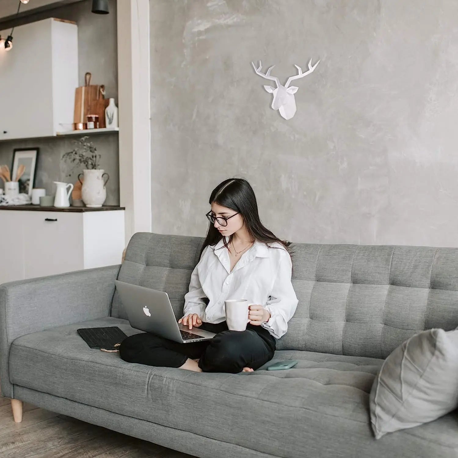 Woman sitting on a gray sofa using a laptop in a modern living room.