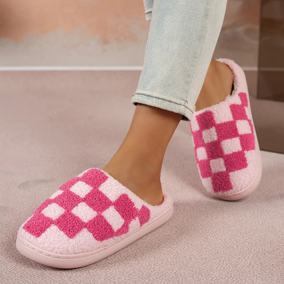 Pink and white checkered slippers worn with light blue jeans on a neutral background