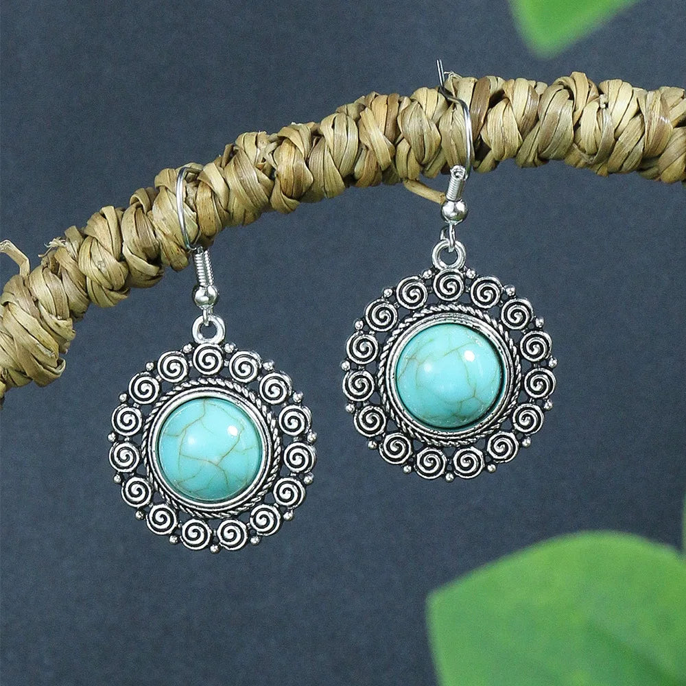 Turquoise earrings with silver intricate designs hanging on a branch against a dark background.