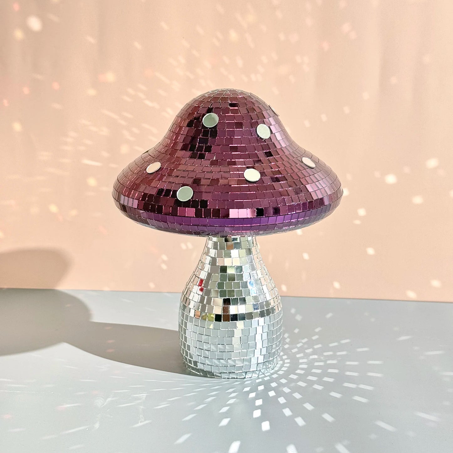 Mushroom-shaped ornament with pink top and silver base on a reflective surface with a soft pink background