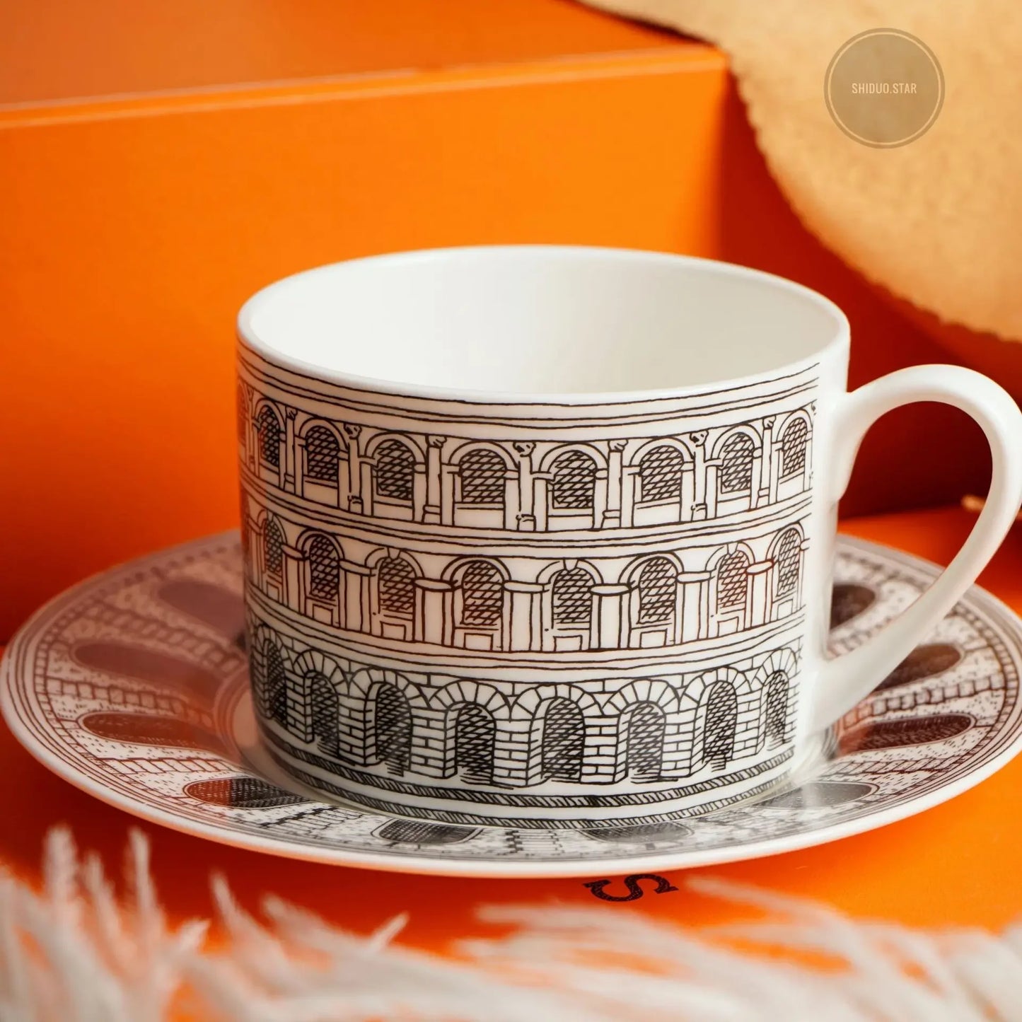 Ceramic cup with architectural design on a saucer against an orange background