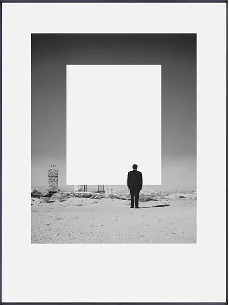 Man standing in a desert landscape with a large rectangular frame in the foreground.