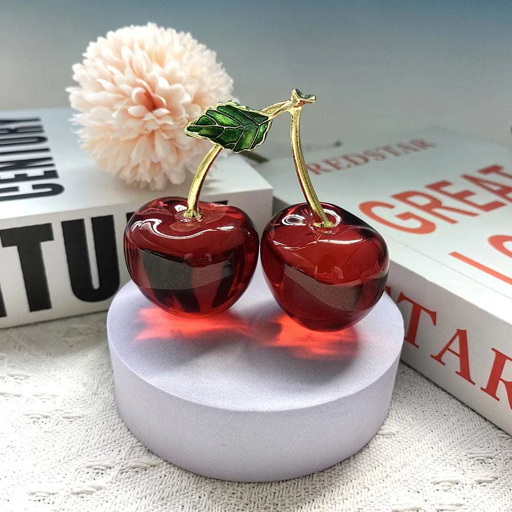 Cherry-shaped ornament on a white round stand with books and a flower in the background
