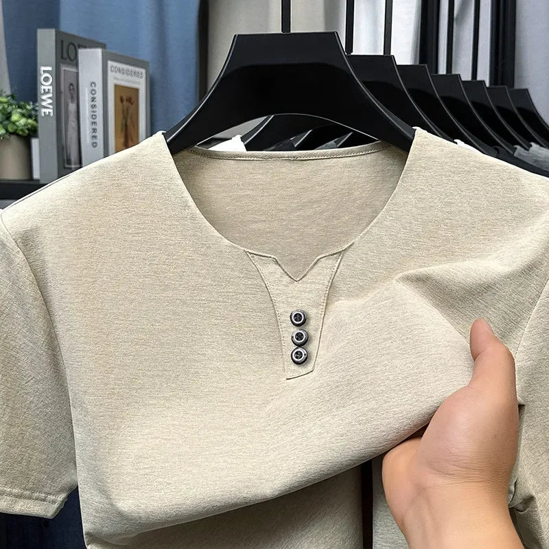 Beige short-sleeve shirt with button details held by a hand against a blurred indoor background.