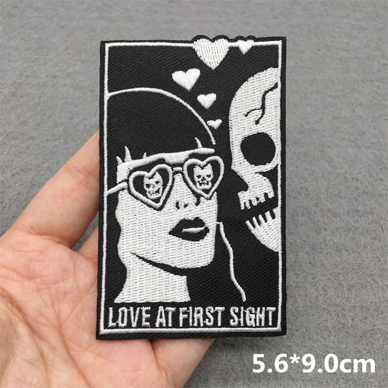 Embroidered patch with skull design and 'Love at First Sight' text held by a hand on a gray background.